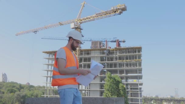 Um engenheiro com um desenho num estaleiro. Jovem engenheiro num estaleiro de construção. Engenheiro num estaleiro de construção — Vídeo de Stock