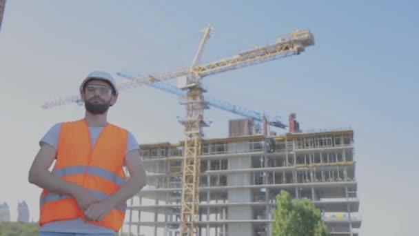 Un ingeniero en una obra de construcción cruza sus brazos sobre su pecho. Ingeniero joven en una obra de construcción. El hombre cruza sus brazos sobre su pecho — Vídeo de stock