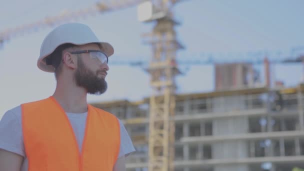 Jovem engenheiro num estaleiro de construção. Um engenheiro com um desenho num estaleiro. Engenheiro num estaleiro de construção — Vídeo de Stock