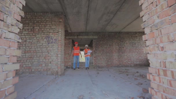 Two builders inside the house. Engineers at the construction of apartment buildings. Two workers in uniform at a construction site — Stock Video