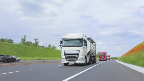 Ciężarówka z cysterną jedzie autostradą w słoneczną pogodę. Konwój ciężarówek jedzie wzdłuż autostrady. Biała ciężarówka jazdy wzdłuż autostrady. — Wideo stockowe