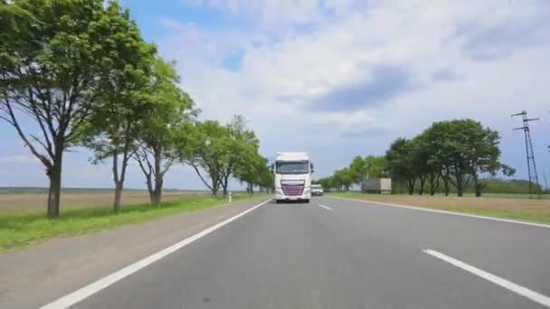 Biała ciężarówka jadąca autostradą. Ciężarówka z cysterną jedzie autostradą w słoneczną pogodę. Konwój ciężarówek jedzie wzdłuż autostrady. — Wideo stockowe