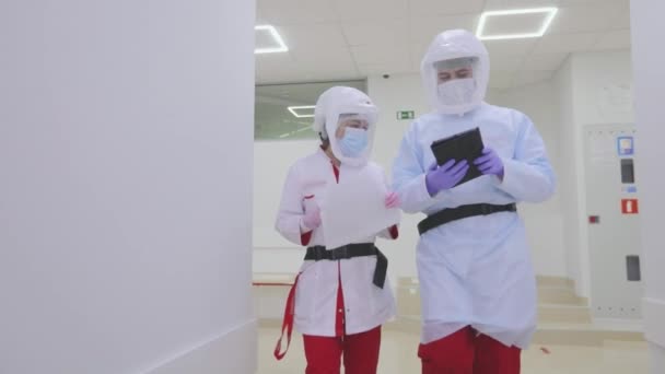 Los médicos con trajes de protección caminan por los pasillos del hospital. Los médicos en protección antiviral están caminando a lo largo de los corredores brillantes del hospital — Vídeo de stock