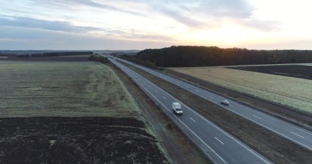 Вантажівка їде на захід сонця по прямій дорозі. Вантажівка їде по дорозі між полями на заході сонця — стокове відео