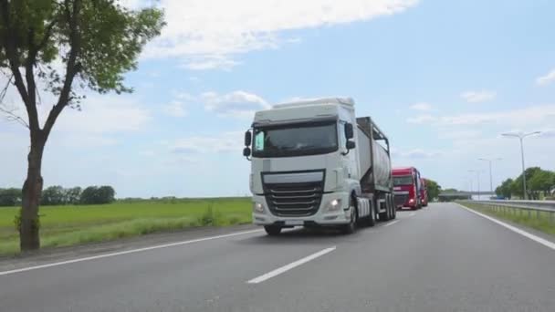 Un camión con un camión cisterna conduce por la carretera en un clima soleado. Un convoy de camiones conduce por la carretera. Camión blanco conduciendo por la carretera. — Vídeo de stock