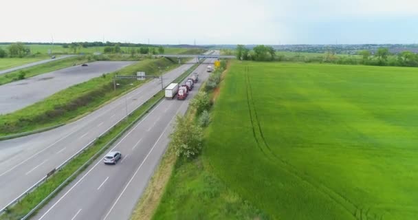 Teherautók lovagol a modern autópályán körül zöld fű tetején kilátás. Teherautók az autópályára néző a drón — Stock videók
