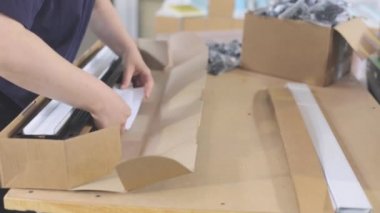 Plastik parçaları bir kutuya koymak. İşçi, müşteriye göndermek için malları bir kutuya koyar.