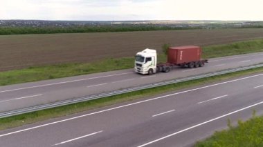 İnsansız hava aracının görüş alanında bir kamyon. Yeşil çimen manzaralı, modern otoyolda kamyon turu. Nakliye. Lojistik