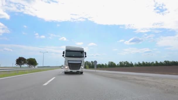 Un camión con un camión cisterna conduce por la carretera en un clima soleado. Un convoy de camiones conduce por la carretera. Camión blanco conduciendo por la carretera. — Vídeo de stock