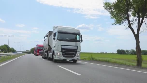 Witte truck rijdt langs de snelweg. Een vrachtwagen met een tanker rijdt bij zonnig weer op de snelweg. Een konvooi vrachtwagens rijdt langs de snelweg — Stockvideo