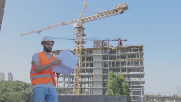 Ein Ingenieur mit einer Zeichnung auf einer Baustelle. Jungingenieur auf einer Baustelle. Ingenieur auf einer Baustelle — Stockvideo