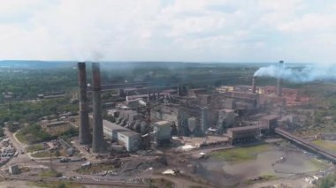 Fabrika insansız hava aracı görüntüsünün bacasından yoğun duman çıkıyor. Dumanı tüten bacası olan büyük bir metal bitkinin üzerinden uçmak. Fabrikanın bacasından duman salınımı.