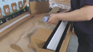 İşçi, müşteriye göndermek için malları bir kutuya koyar. Bir kutuda plastik parçalar paketleniyor.