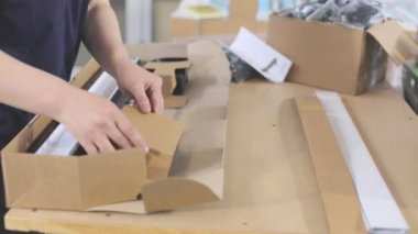 Plastik parçaları bir kutuya koymak. İşçi, müşteriye göndermek için malları bir kutuya koyar.