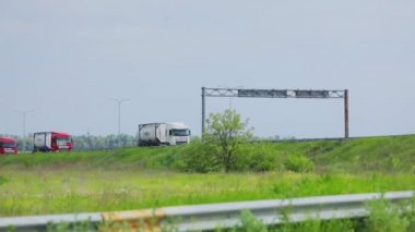 Kamyonlar yol boyunca gidiyor. Bir kamyon konvoyu otobanın altından geçiyor. Pistteki modern kamyonlar