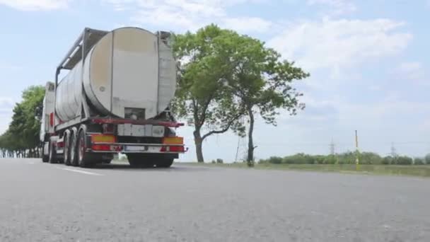 Fehér teherautó halad az autópálya mentén. Egy kamion tankhajóval az autópályán, napos időben. Egy teherautó konvoj halad végig az autópályán. — Stock videók