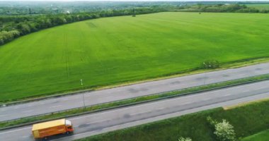 Yeşil tarlanın yakınındaki yolda giden turuncu kamyon. Kamyon otoyolda gidiyor. Kamyon otoban manzarası boyunca gidiyor.