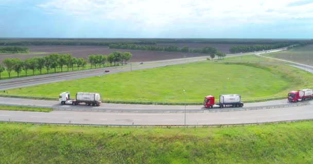 Los camiones están conduciendo a lo largo de la carretera cerca del campo verde. Camiones cisterna conduciendo por la carretera. Camiones conduciendo a lo largo de la carretera vista superior — Vídeo de stock