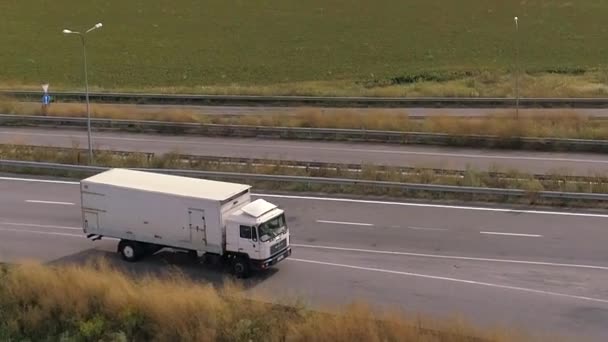 Ciężarówki jazdy na nowoczesnej autostradzie wokół zielonej trawy widok z góry. Ciężarówka na autostradzie widok z drona. — Wideo stockowe