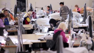 Birçok terzi bir giyim fabrikasında çalışır. Bir giyim fabrikasında çalışma süreci. Büyük dikiş atölyesi. Terziler fabrikada ürün yapar. Kumaş fabrikası