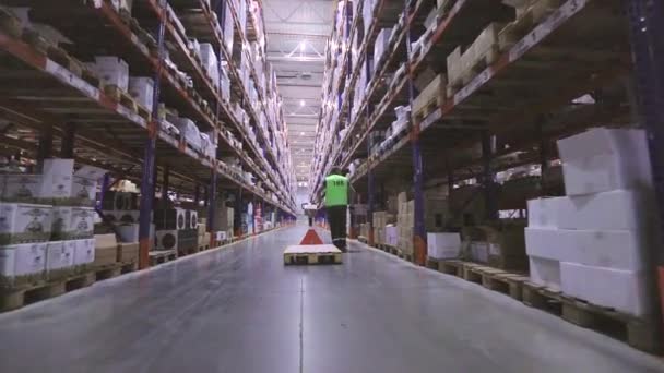 Dělník vozí zboží na vysokozdvižném vozíku. Muž ve velkém skladišti nese zadní pohled na hydraulický paletový vozík. Dělník ve skladišti. Velký moderní sklad — Stock video