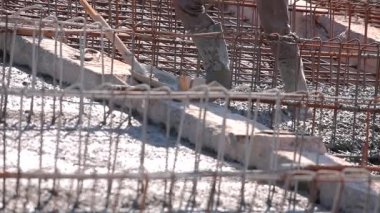 Metal bir yapıya beton dökülüyor. İşçiler güçlendirilmiş beton yapı yapıyorlar. Güçlendirilmiş beton. İnşaat alanında çalışma süreci