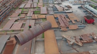 Büyük metal bir boru bir vinç tarafından kaldırılır. Metal yapıların montajı için bir fabrika. Metal yapılar montajı için atölyenin üzerinden uçuyor. Endüstriyel dış görünüş. Üst görünümü yerleştir