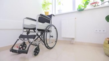 Beyaz koridorda engelliler için tekerlekli sandalye. Hastane koridorunda engelliler için boş tekerlekli sandalye. Parlak bir pencerenin arka planında boş tekerlekli sandalye