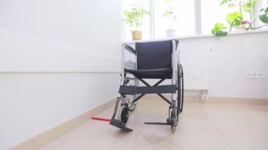 Beyaz koridorda engelliler için tekerlekli sandalye. Hastane koridorunda engelliler için boş tekerlekli sandalye. Parlak bir pencerenin arka planında boş tekerlekli sandalye
