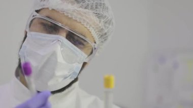 Bilim adamı plan için test tüplerine bakıyor. Laboratuvar test tüpleri yakın plan, arka plandaki bilim adamının yüzü.