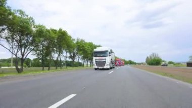 Tankerli bir kamyon güneşli havada otoyola çıkıyor. Bir kamyon konvoyu otoyol boyunca sürer. Otoyol boyunca giden beyaz bir kamyon..