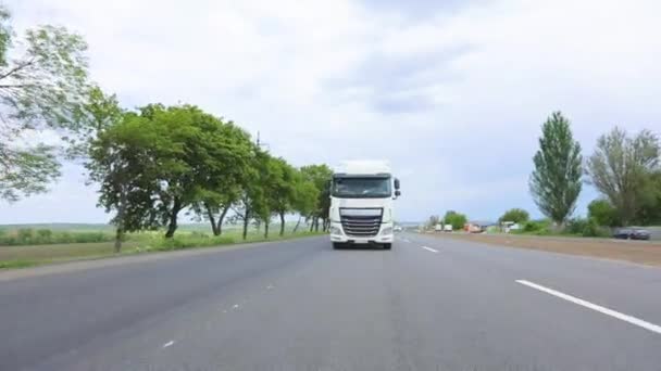 Un camión con un camión cisterna conduce por la carretera en un clima soleado. Un convoy de camiones conduce por la carretera. Camión blanco conduciendo por la carretera. — Vídeos de Stock
