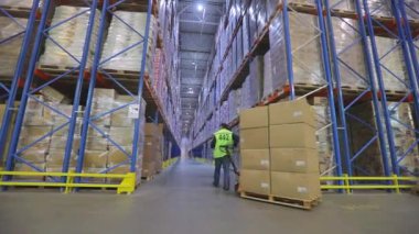 Büyük bir depoda bir adam hidrolik bir araba taşıyor. Depoda bir adam bir rokla taşıyor. Depo işçisi. Büyük modern depo