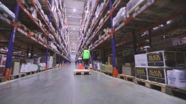 Büyük bir depodaki bir adam hidrolik palet kamyonunun arka camını taşıyor. Bir işçi forkliftle mal taşır. Depo işçisi. Büyük modern depo