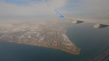 Uçak ile şehir üzerinde uçmak. Uçak penceresinden görülen şehir yolcu penceresinden görülüyor. Uçak penceresi manzaralı. Uçak penceresinin dışını göster.