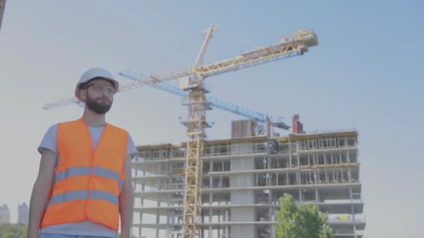 Ingeniero joven en una obra de construcción. Un ingeniero con un dibujo en un sitio de construcción. Ingeniero en una obra de construcción — Vídeo de stock