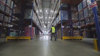 Bir adam ambarın arkasından yavaş çekimde yürür. Bir işçi fabrika deposundan geçiyor. Depoda yürüyen bir işçinin arkadan görünüşü