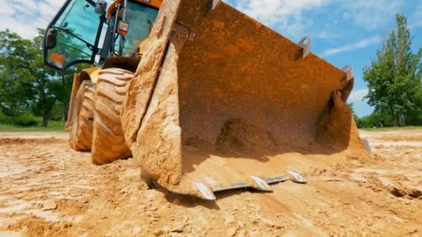 Cubo del tractor de cerca. Un tractor cava un agujero en un sitio de construcción. Proceso de trabajo en una obra. — Vídeos de Stock