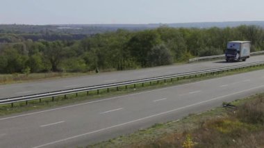 Bir kargo kamyonu otoyol boyunca gidiyor. İnsansız hava aracı görüntüsü. Vagon, tarlaların üst manzarası arasında virajlı bir yolda ilerliyor.