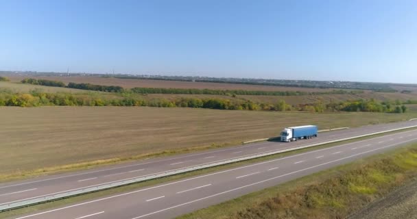 A teherautó egy hosszú, egyenes úton halad. A teherautó az úton halad, a természet körülötte van. Kocsi halad végig az úton drónlövések — Stock videók