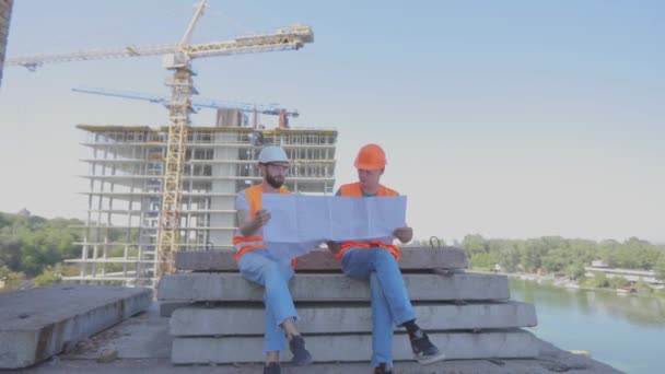 Ingenieros en el fondo del sitio de construcción marco divertido. Ingenieros de tiros cómicos cruzan sus piernas. — Vídeos de Stock