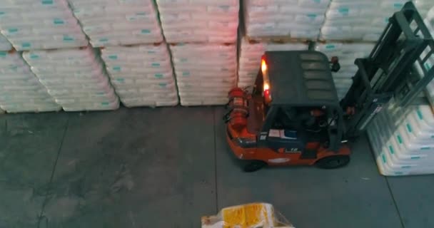 A forklift works in a warehouse. A forklift in a warehouse moves white bags. Forklift transports goods. White bags in a factory warehouse — Stock Video