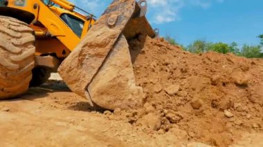 Bir traktör inşaat alanında çukur kazıyor. İnşaat alanında çalışma süreci. Traktör kovası yaklaş.