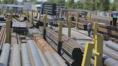Metalle dolu bir depoda çalışma süreci. İşçiler vinç altında duran bir kamyona metal yüklüyorlar, işçiler rampada. Bir kamyonu gantry vinçle yüklemek