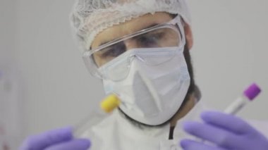 Bilim adamı plan için test tüplerine bakıyor. Laboratuvar test tüpleri yakın plan, arka plandaki bilim adamının yüzü.