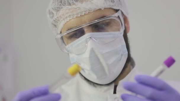 O cientista olha para os tubos de ensaio para o plano. tubos de ensaio de laboratório close-up, a face do cientista em segundo plano — Vídeo de Stock