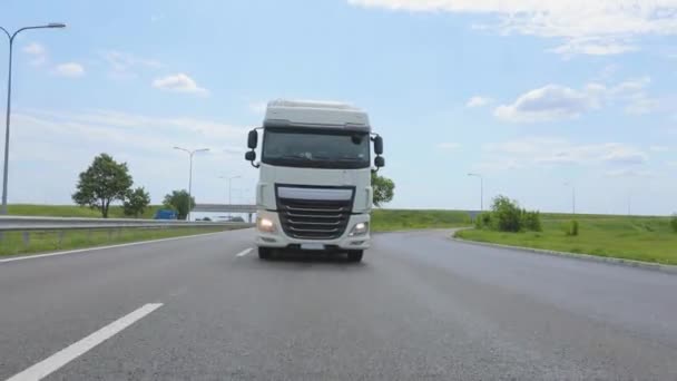 Camión blanco conduciendo por la carretera. Un camión con un camión cisterna conduce por la carretera en un clima soleado. Un convoy de camiones recorre la carretera — Vídeo de stock