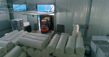 Depodaki bir forklift beyaz çantaları taşır. Bir forklift depoda çalışır. Dolgu malzemesi ruloları. Ekmekte Spunbond