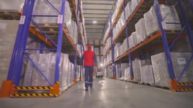 Bir işçi modern bir depoda yürüyor. Depo işi. Depoya bakan bir adam var..