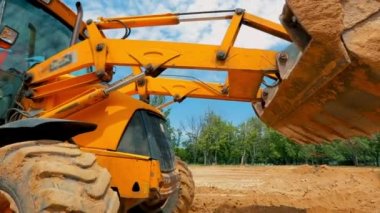 Bir traktör inşaat alanında çukur kazıyor. İnşaat alanında çalışma süreci. Traktör kovası yaklaş.